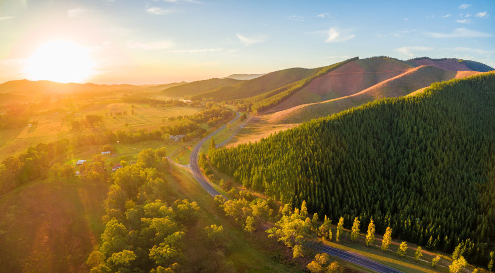 Aerial panorama of sunset over countryside - winding road, forested hills and golden colors